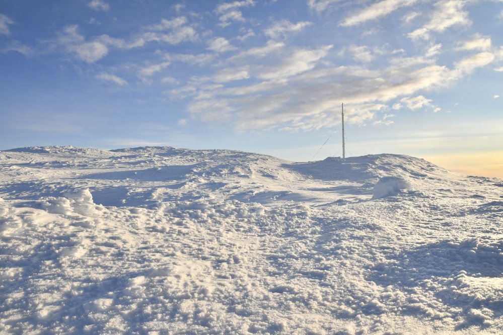 Tasaisempaa lumista tunturimaastoa Saanan huipulla, Saanan maston näkyessä taustalla