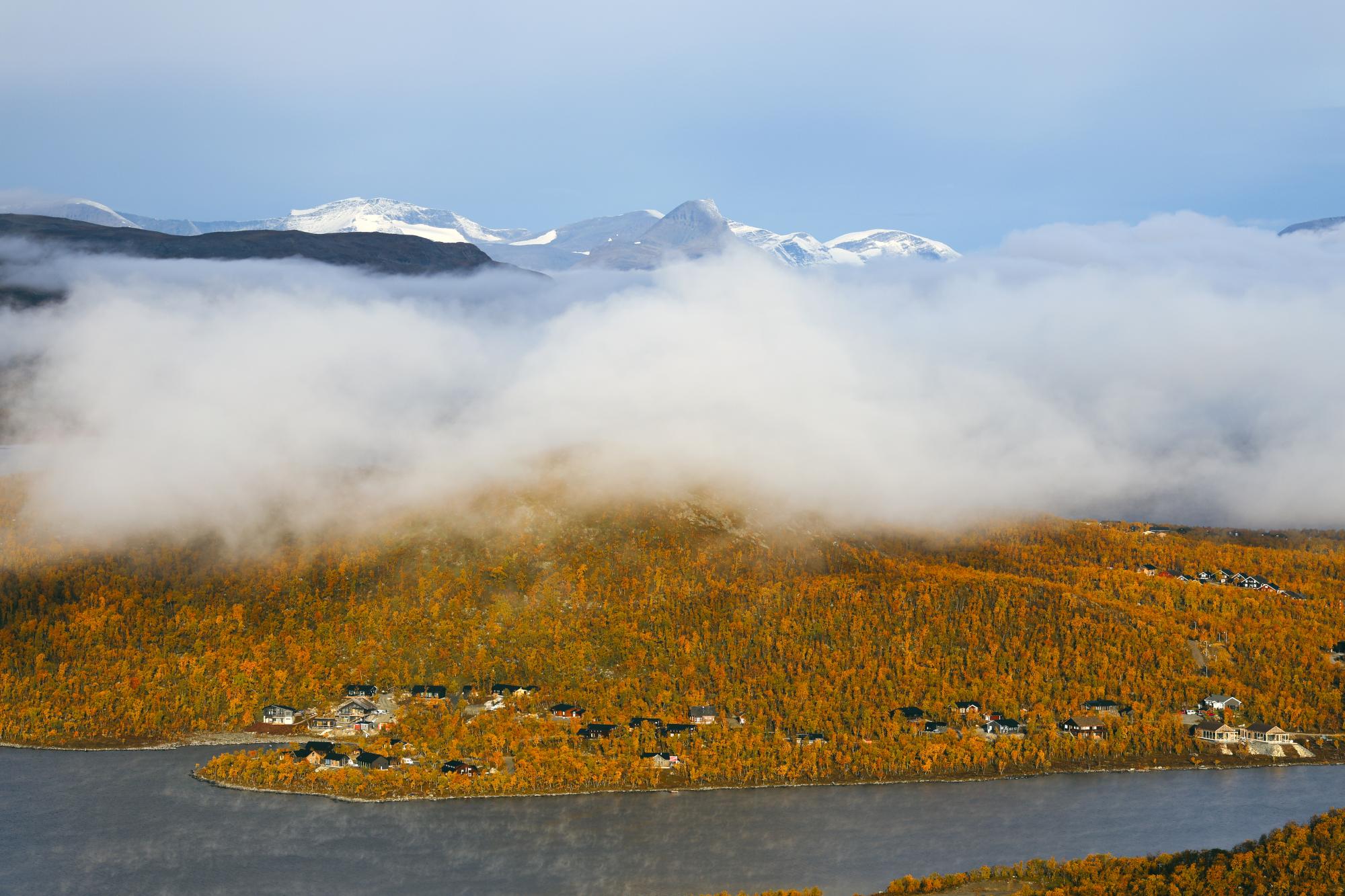Salmivaara fell rises above Kilpisjärvi, glowing in the colours of autumn. The summit is wrapped in mist, while Norway’s Barras mountain appears in the background.unturi
