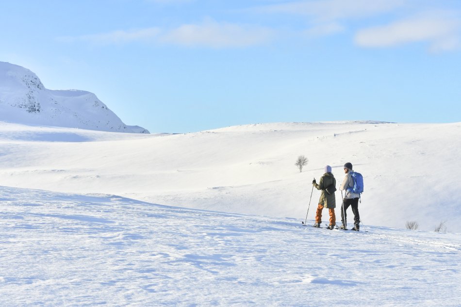 Two people skiing on Kilpisjärvi’s sunny spring snowfields with skis rented from Kilpisjärven Retkeilykeskus