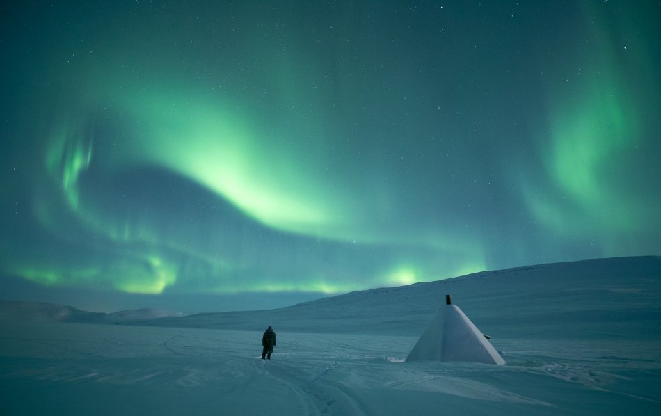 A person standing in snow beneath northern lights in Kilpisjärvi