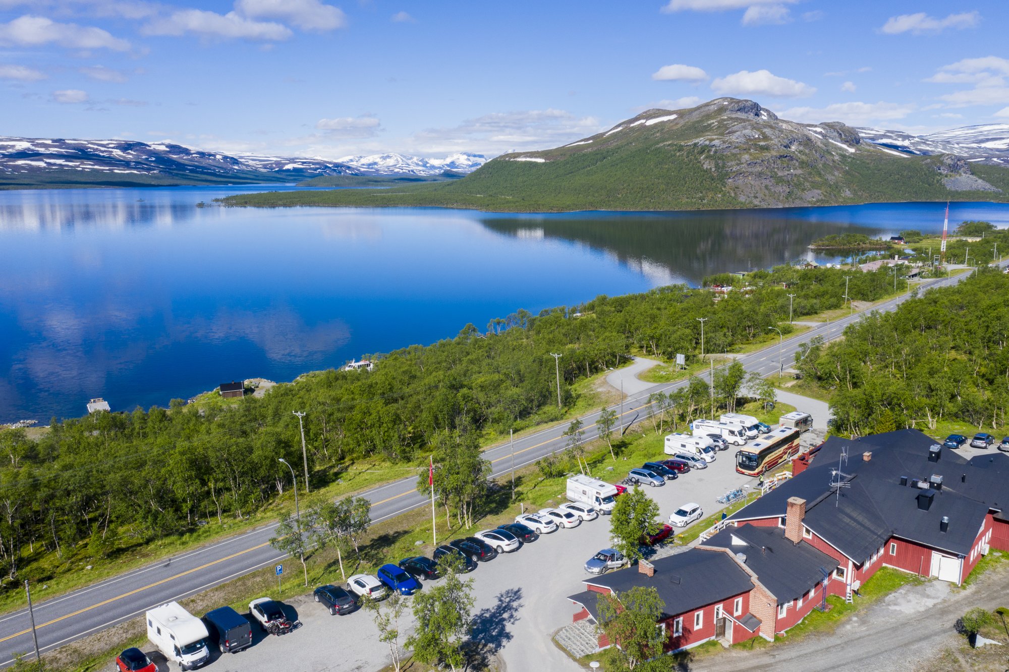 The image shows Kilpisjärven Retkeilykeskus in Lapland Finland on a summer day by the mirror-calm shores of Lake Kilpisjärvi.