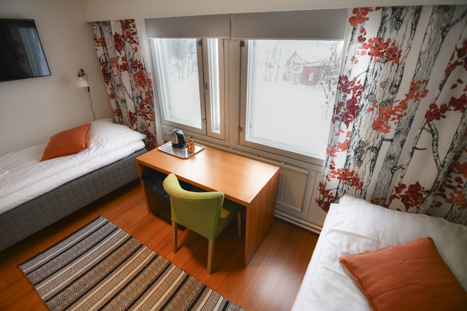 Twin room in Kilpisjärven Retkeilykeskus. Two beds, a desk, chair, tv and a fridge.