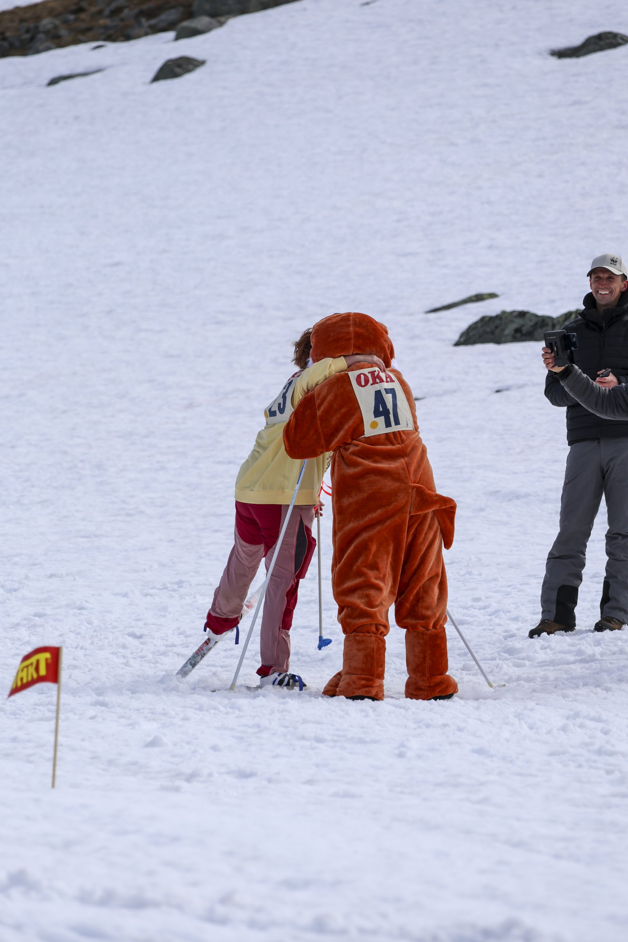 Kuvassa nallemaskotti halaa Kilpisjärven juhannushiihdoissa maaliin hiihtänyttä osallistujaa