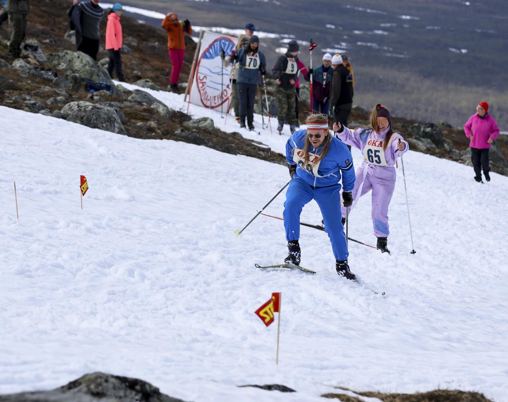 Kuvassa on retroasuihin pukeutunut mies ja nainen, jotka hiihtävät kilpaa Kilpisjärven juhannushiihdoissa