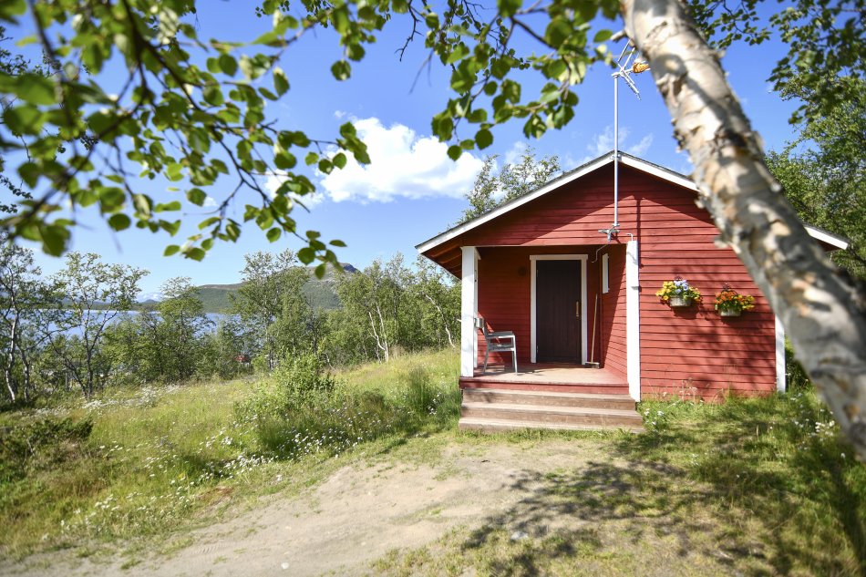Red cabin in the summertime in Kilpisjärvi with green leaves and trees