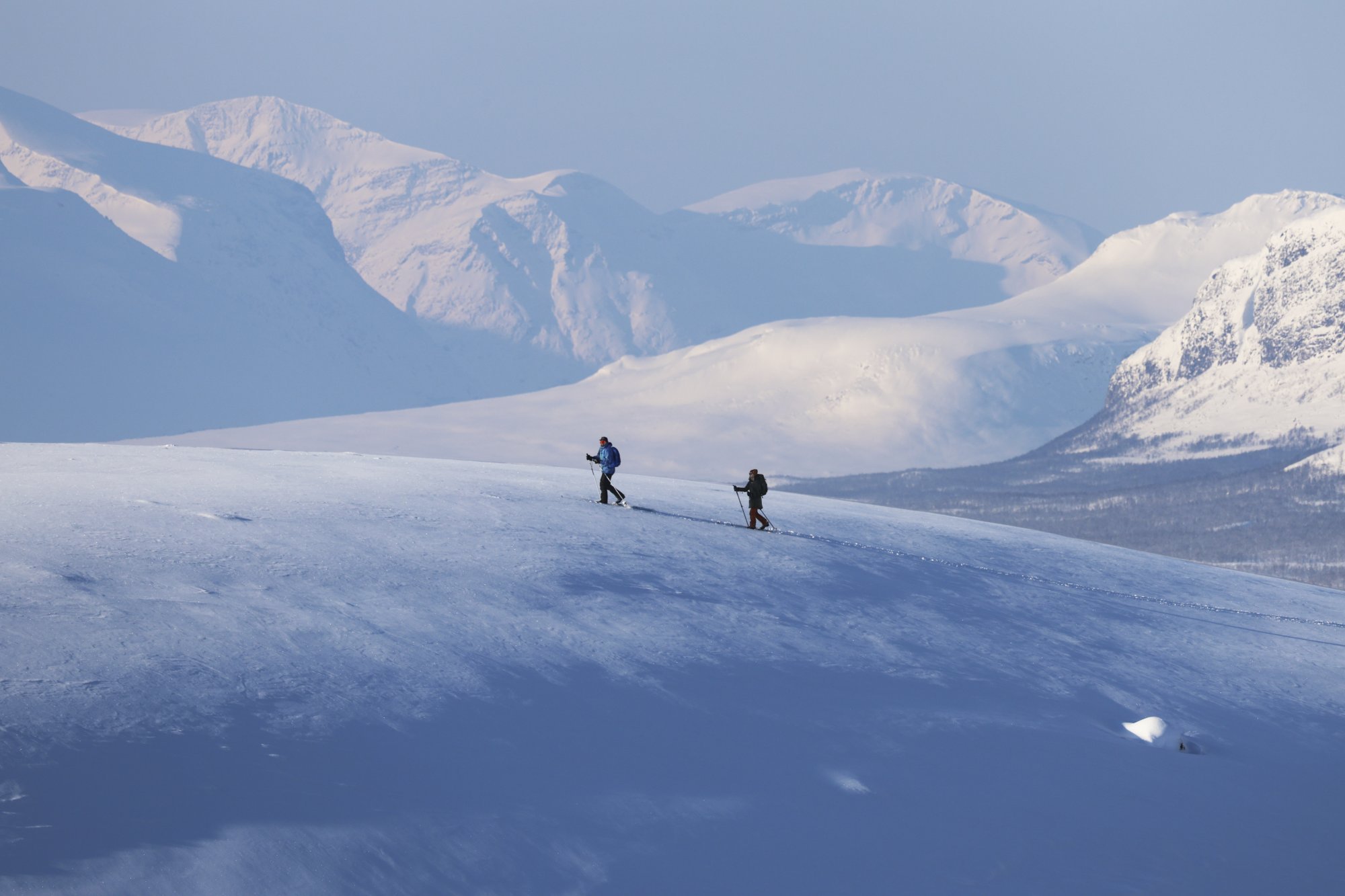 A man and woman skiing in Kilpisjärvi with mountains behind them